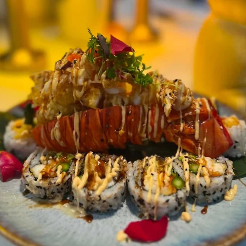 Katsumori's lobster sushi roll, garnished with herbs and red petals, on a light blue plate.