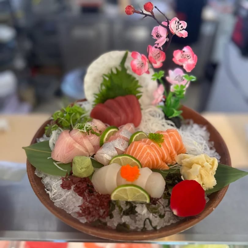 A platter of Katsumori Asian Fusion sashimi with tuna, salmon, and other fish, garnished with limes and flowers.